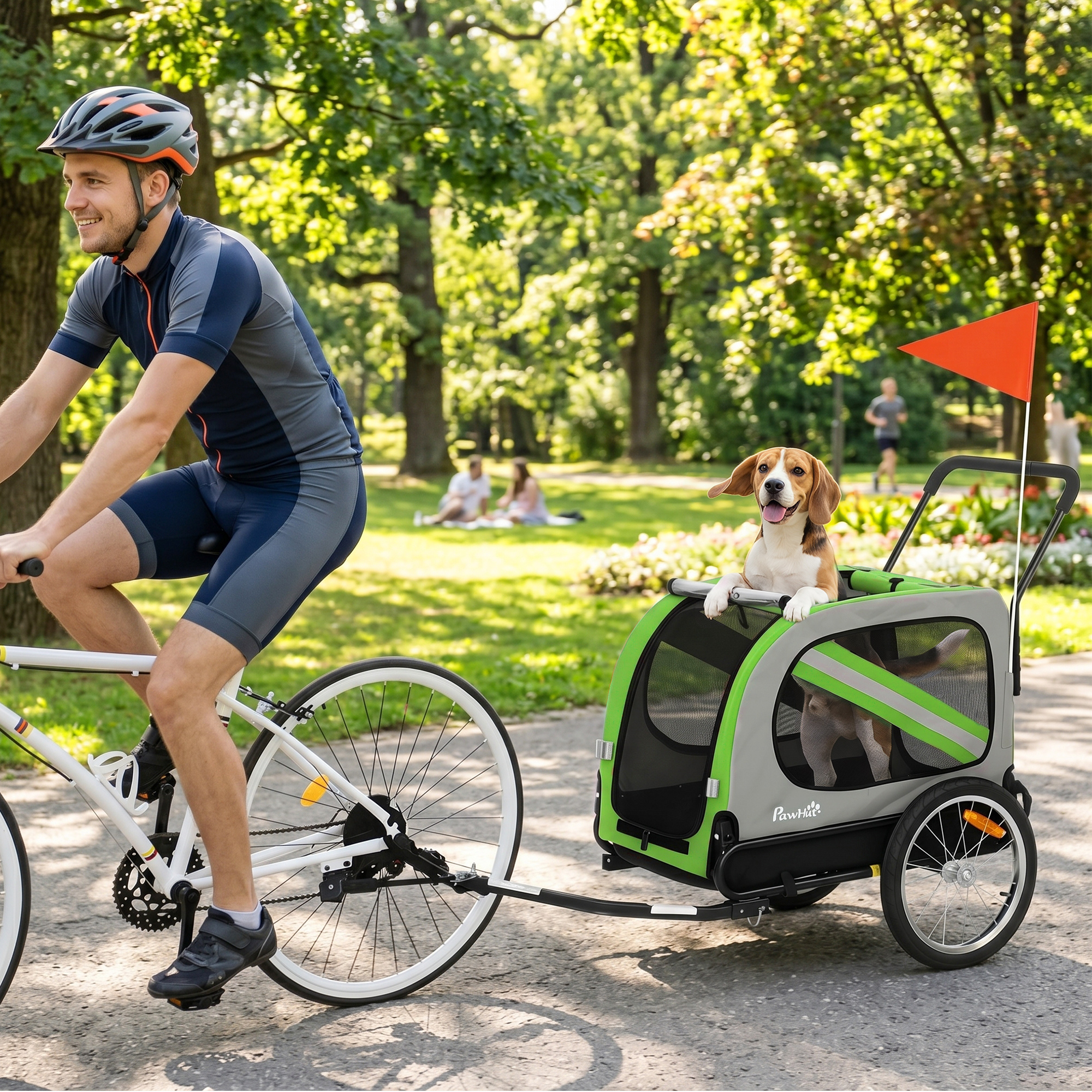 Un hombre en bicicleta arrastra un remolque verde y gris para mascotas con un beagle adentro en un parque.