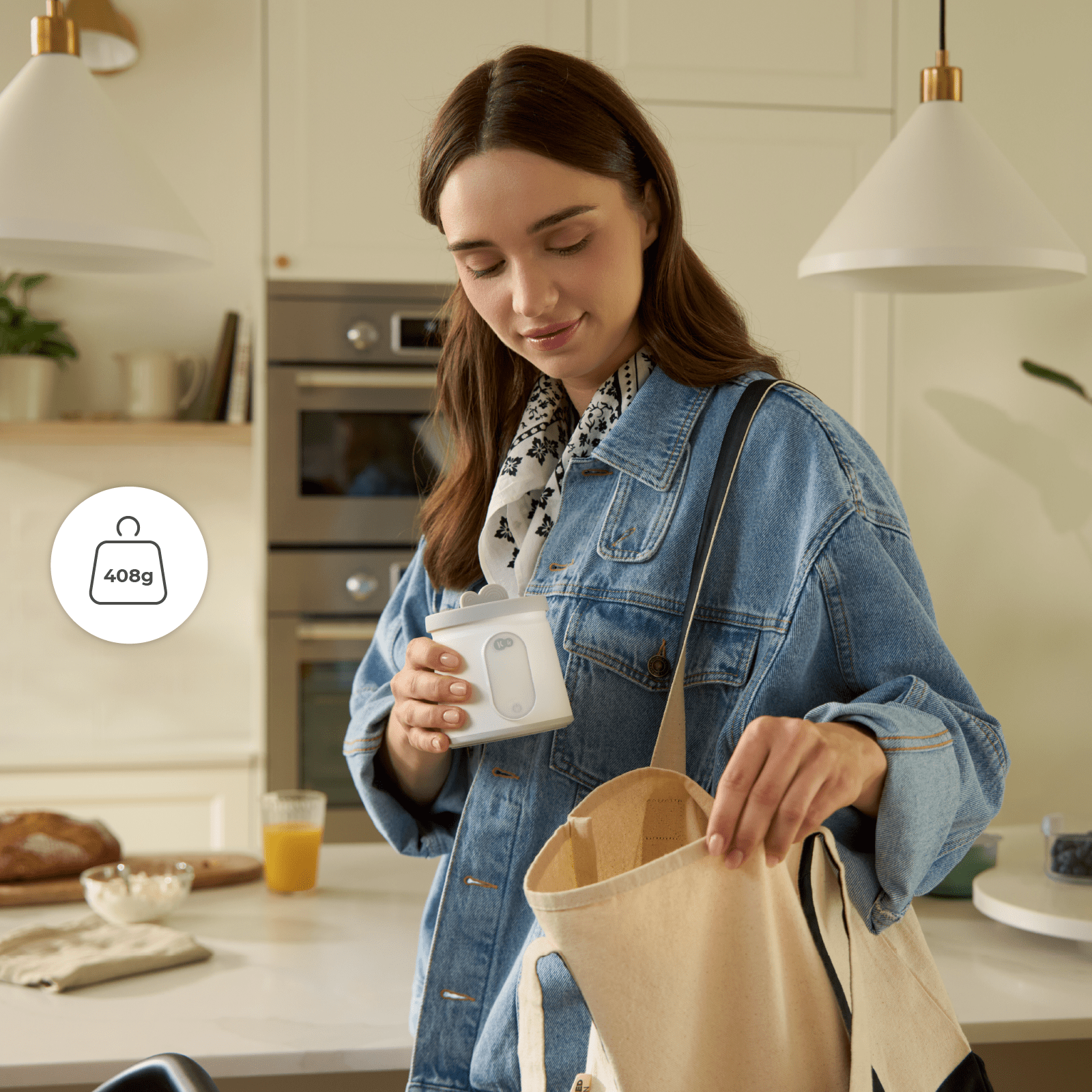 Eine Frau in Jeansjacke stellt in einer hellen Küche einen kleinen weißen Behälter in eine Stofftasche.