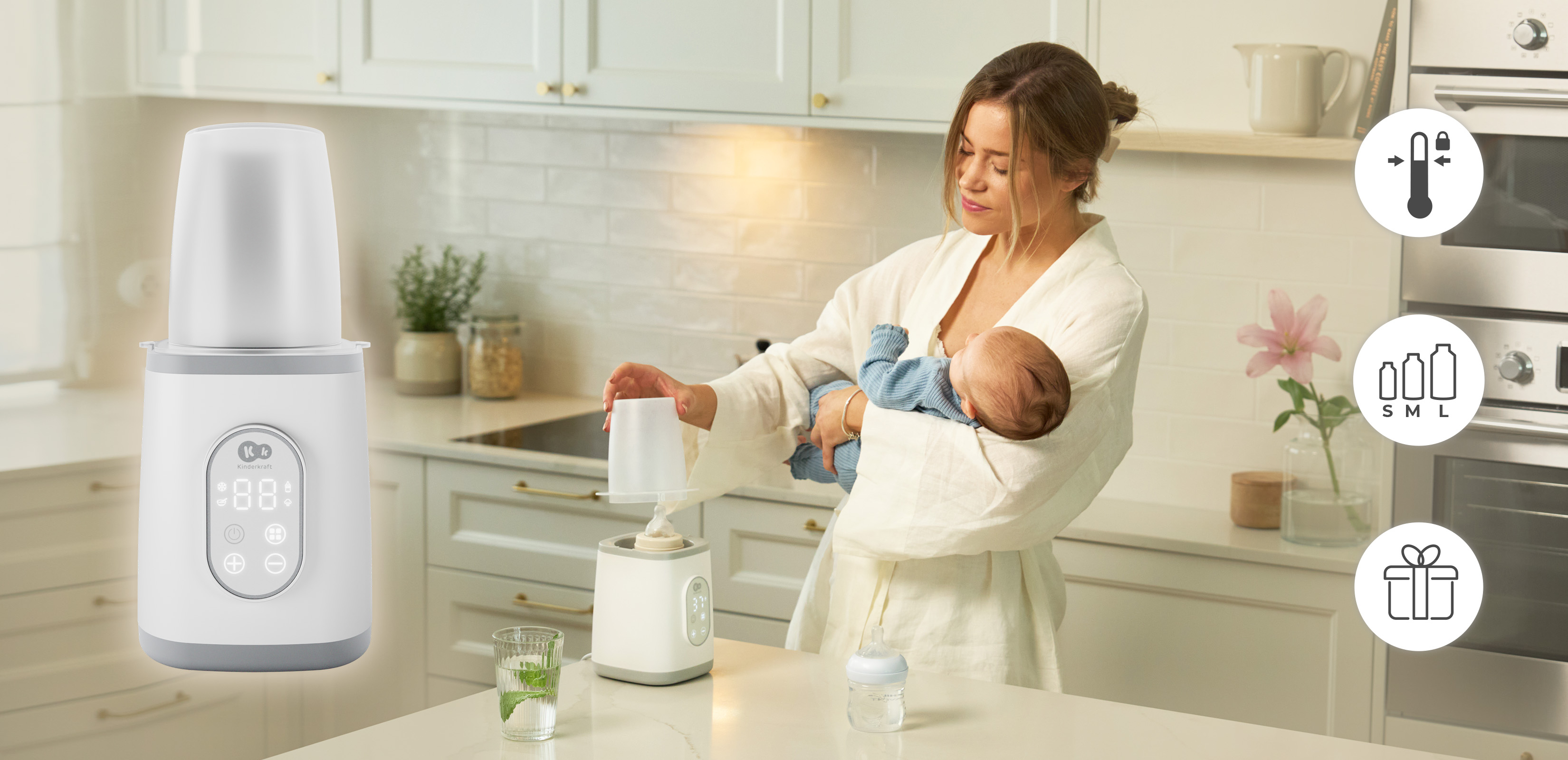 Eine Frau im weißen Bademantel hält ein Baby und bedient einen weißen Babyflaschenwärmer in der Küche.