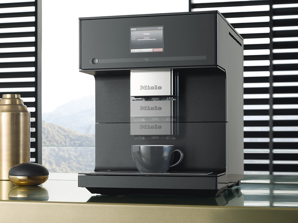 Moderne schwarze Miele-Kaffeemaschine mit digitalem Display und gefüllter Tasse auf einem Tisch.