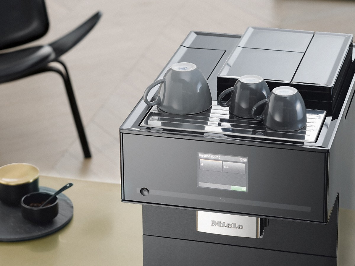 Eine schwarze Miele Kaffeemaschine mit drei grauen Tassen auf der Wärmer und einem Display.