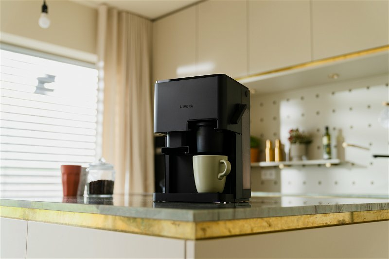 Una macchina da caffè nera si trova su un bancone da cucina con una tazza verde chiaro in una cucina moderna.