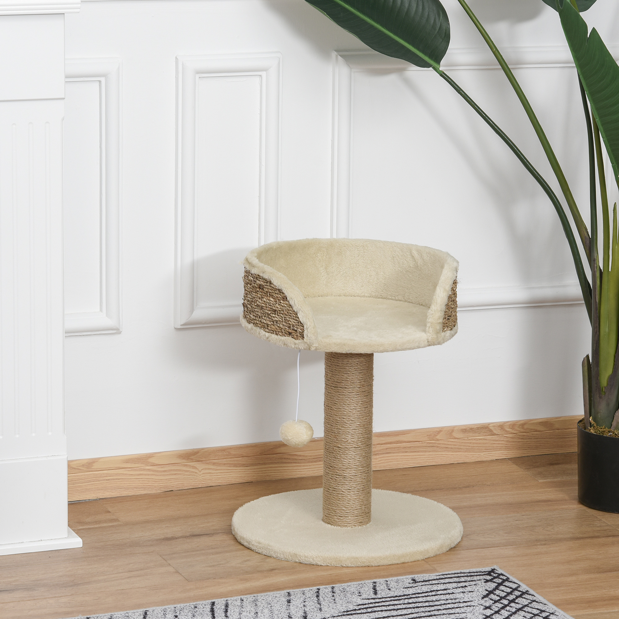 Un rascador para gatos beige con poste de sisal y cama frente a una pared blanca y una planta grande.