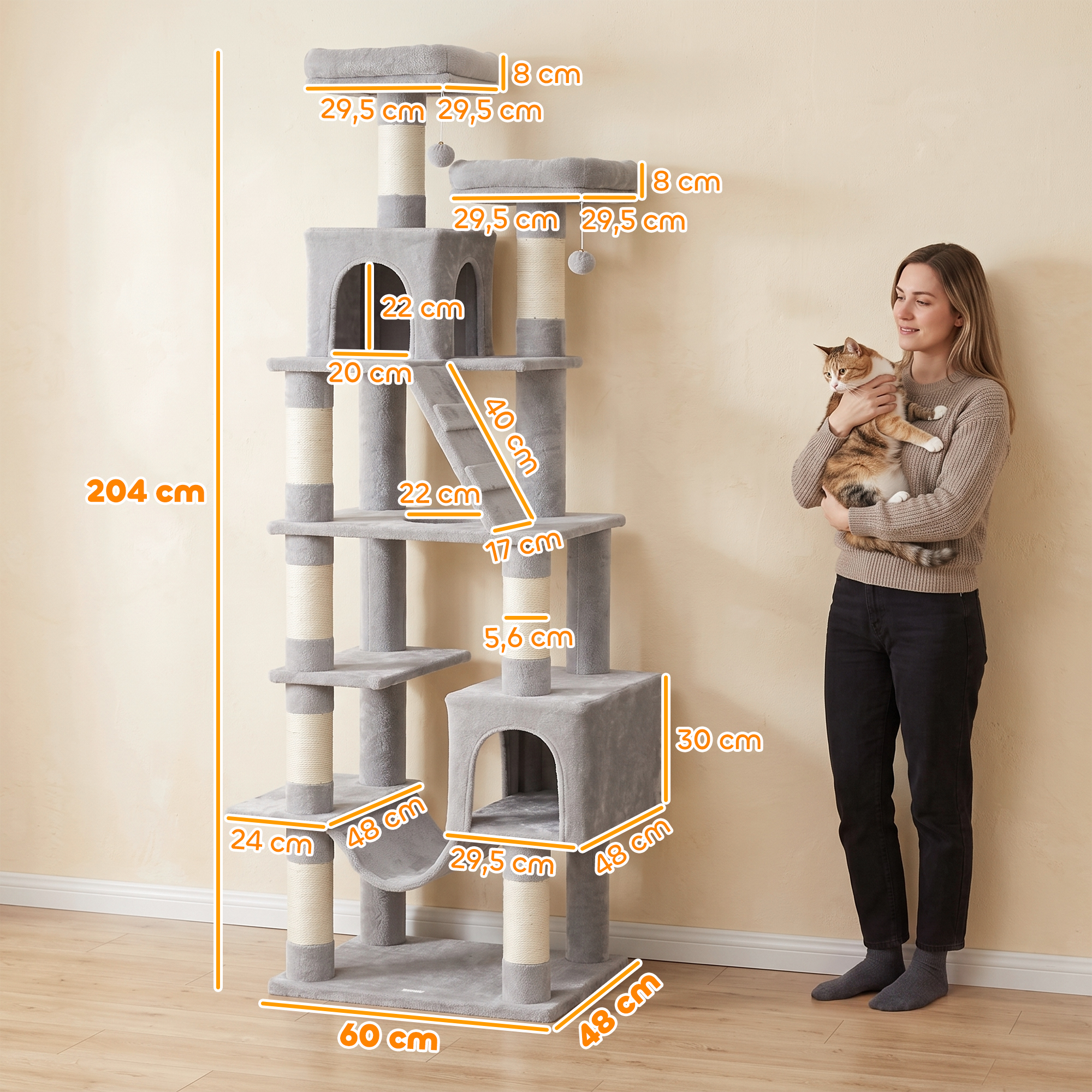 Una mujer sostiene un gato junto a un gran árbol para gatos gris con medidas.