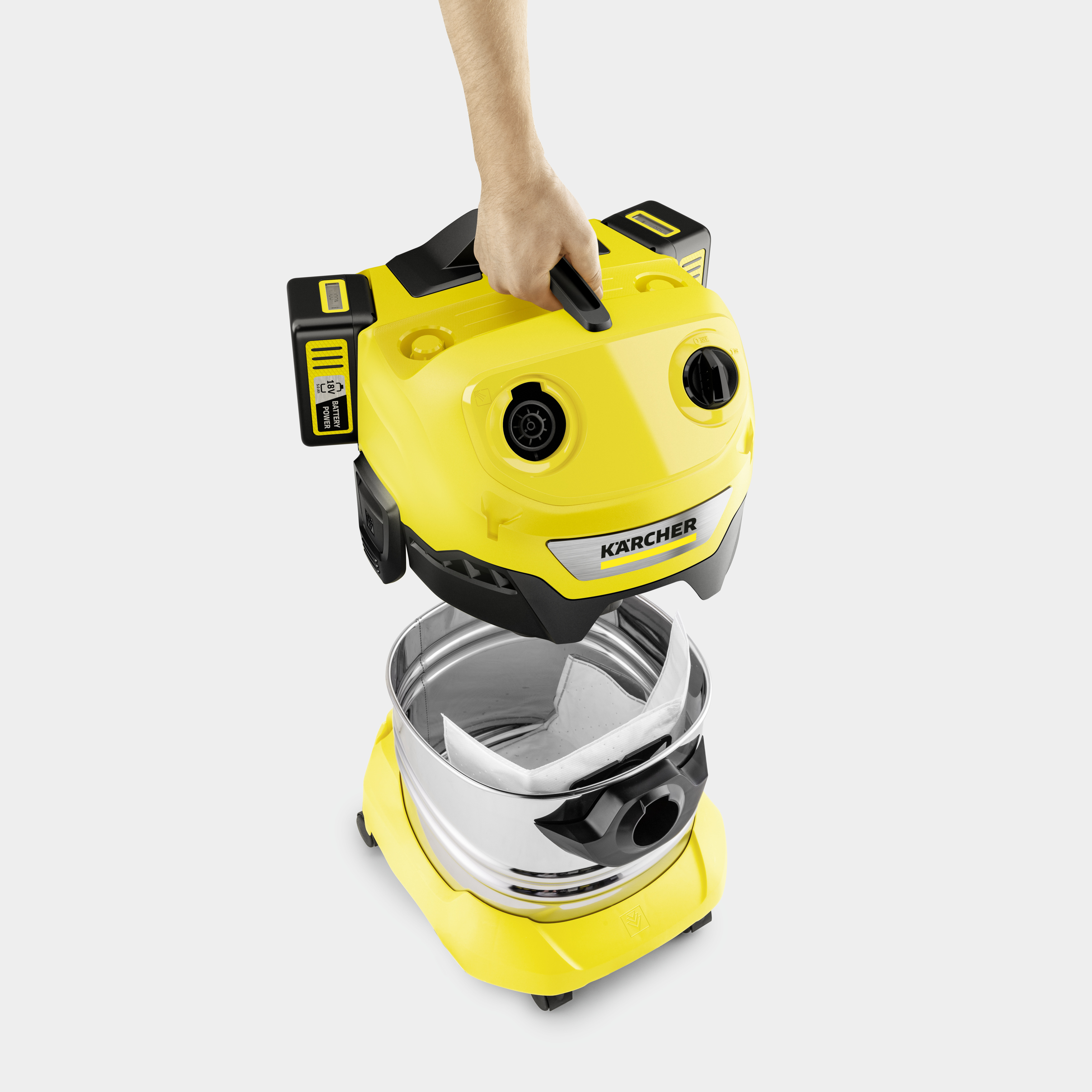 Una mano solleva la parte superiore gialla di un aspirapolvere Karcher dal contenitore in acciaio.