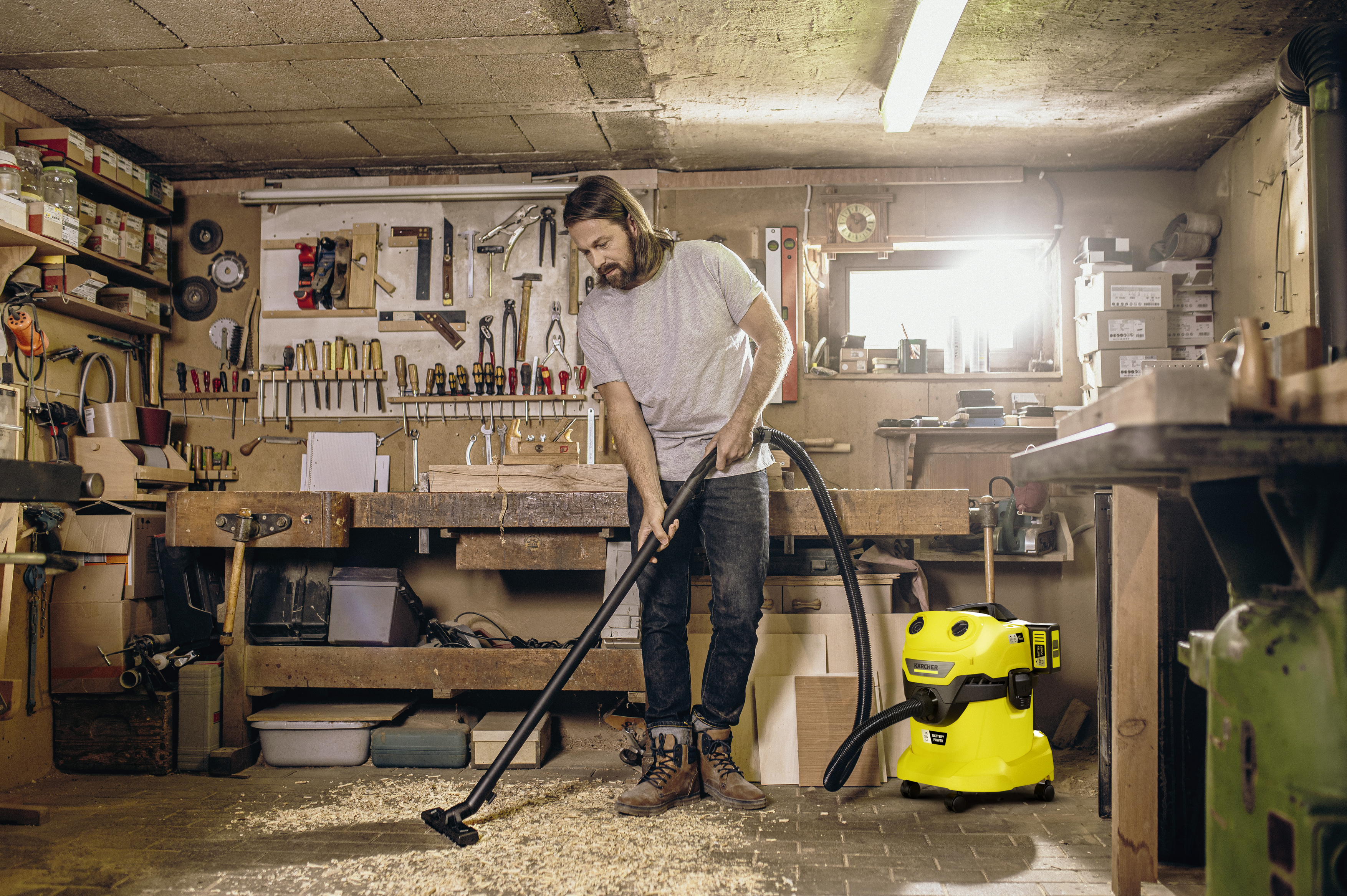 Un uomo usa un aspirapolvere giallo per pulire la segatura in un'officina.