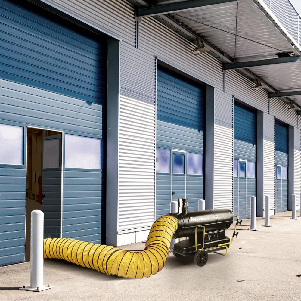 Un calefactor industrial portátil con manguera amarilla frente a un almacén con puertas azules.