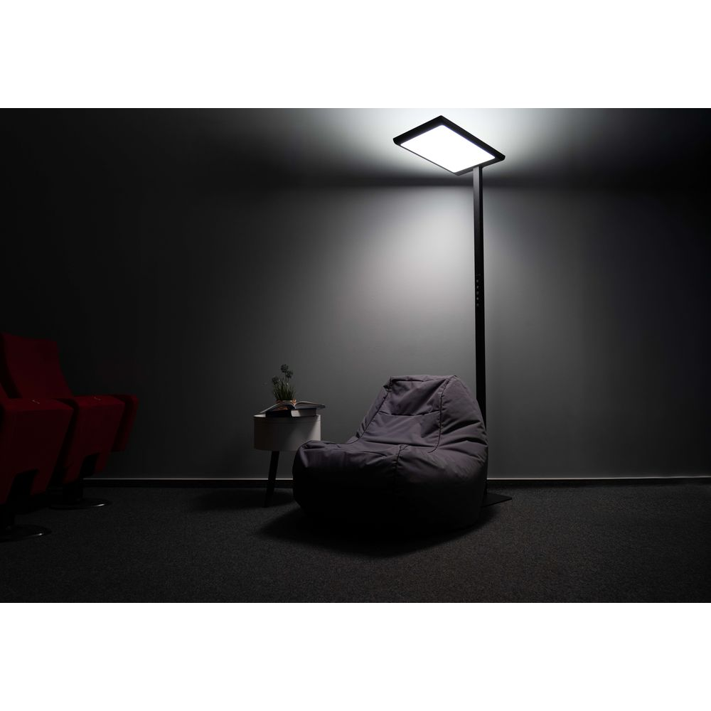 Ein grauer Sitzsack und eine helle Stehlampe in einem dunklen Raum mit einem kleinen Tisch.