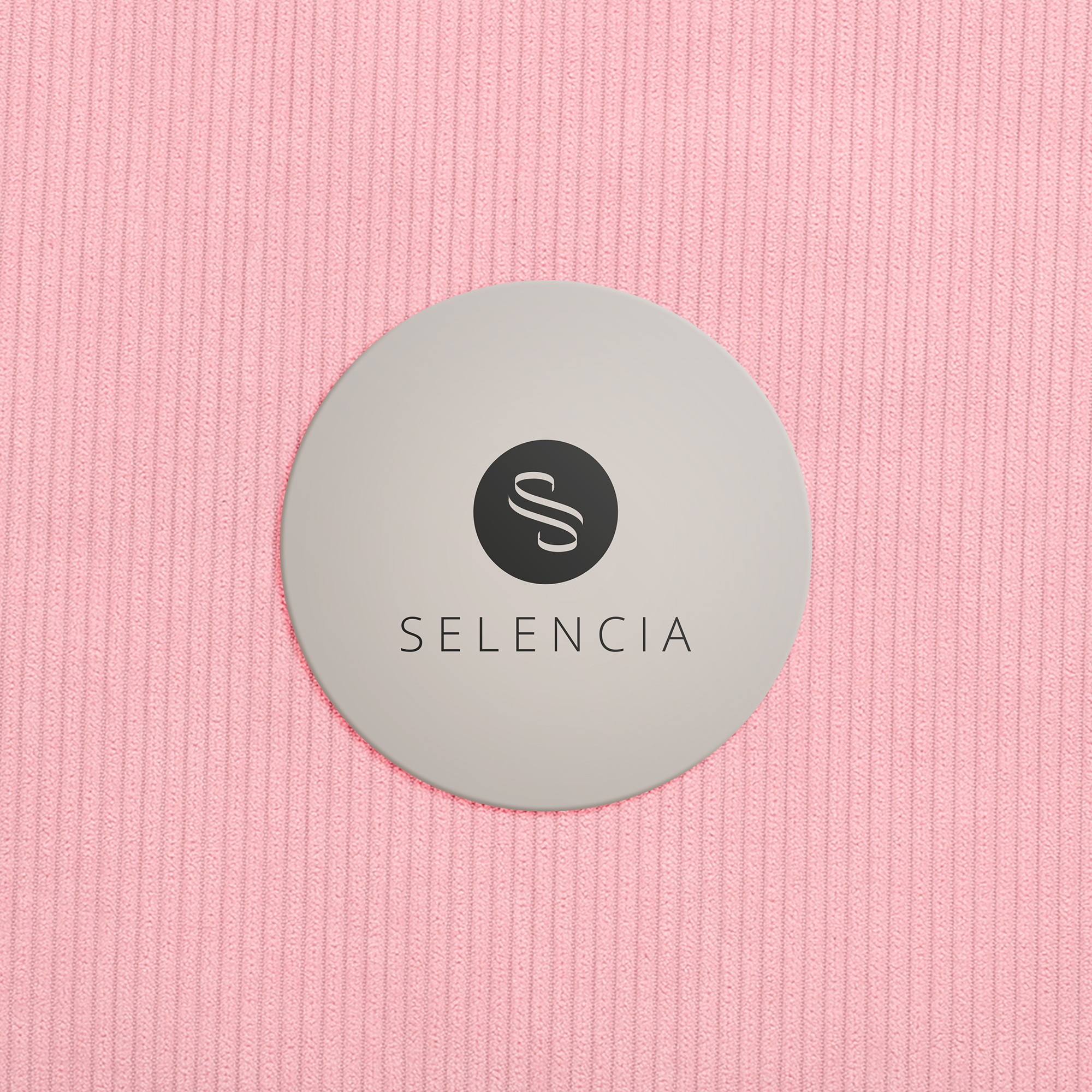 Ein rundes, graues Etikett mit dem Markennamen Selencia liegt auf einem strukturierten, rosa Stoff.