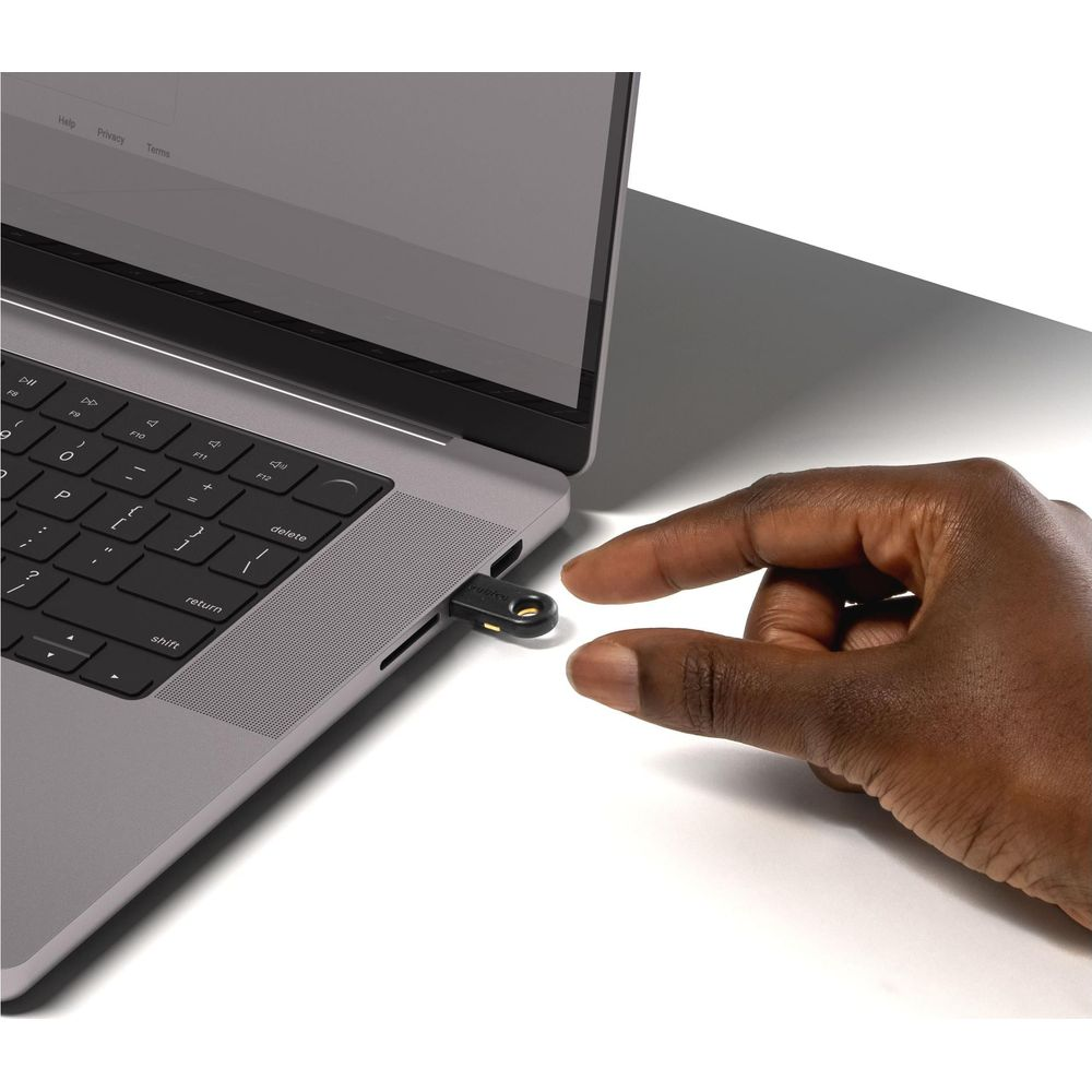 Eine Hand steckt einen kleinen schwarzen USB-Sicherheitsschlüssel in den Port eines grauen Laptops.