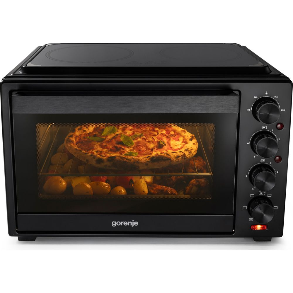 Un mini forno nero Gorenje cuoce pizza e patate all'interno illuminato, con manopole rotanti sul pannello laterale.