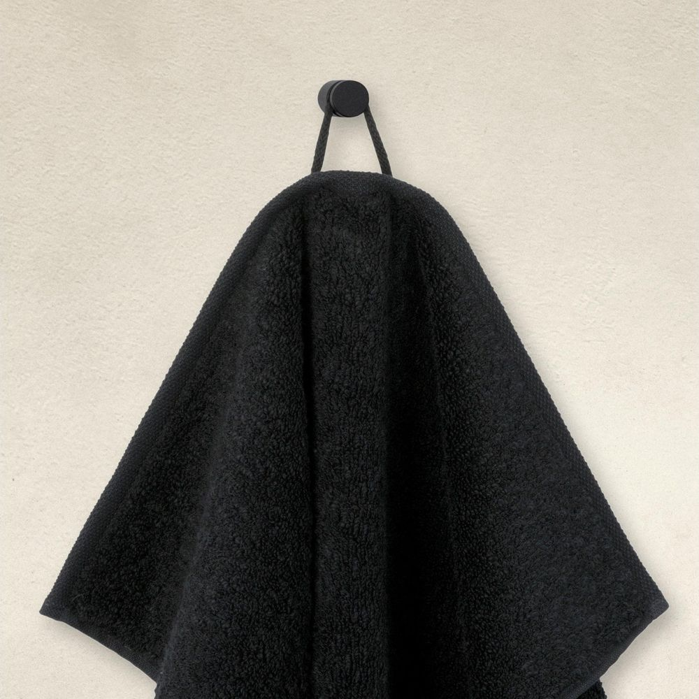 Ein schwarzes Handtuch hängt an einer Kordel an einem schwarzen Haken vor einer hellen Wand.