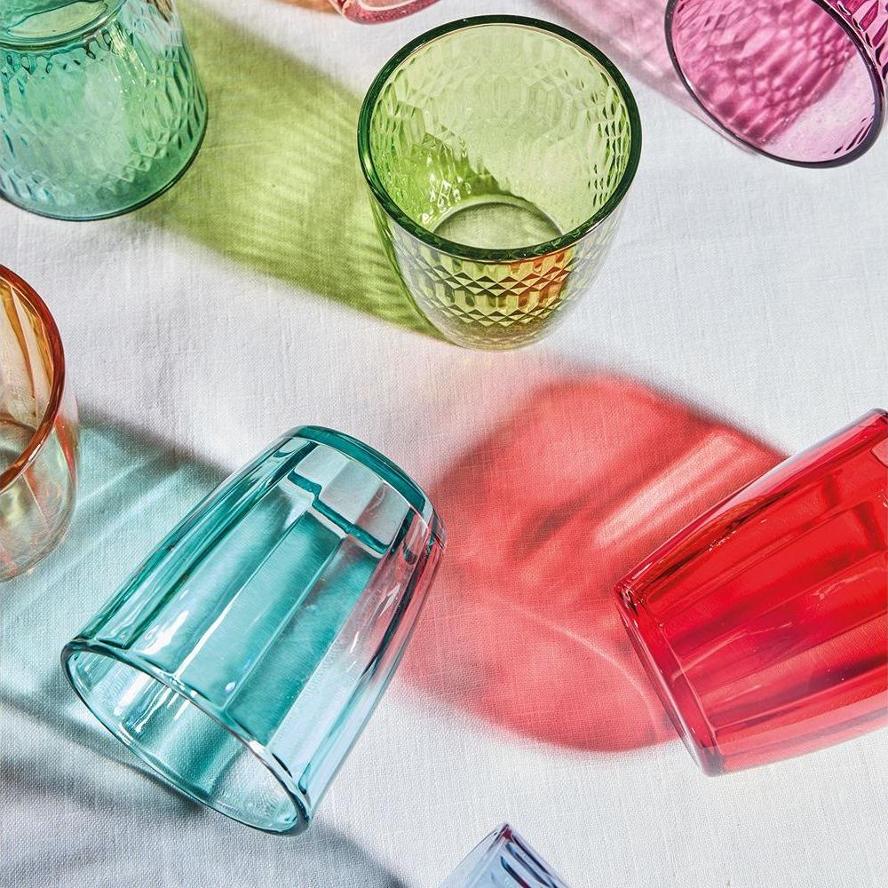 Bunte, strukturierte Gläser werfen helle Schatten auf eine weiße Tischdecke.