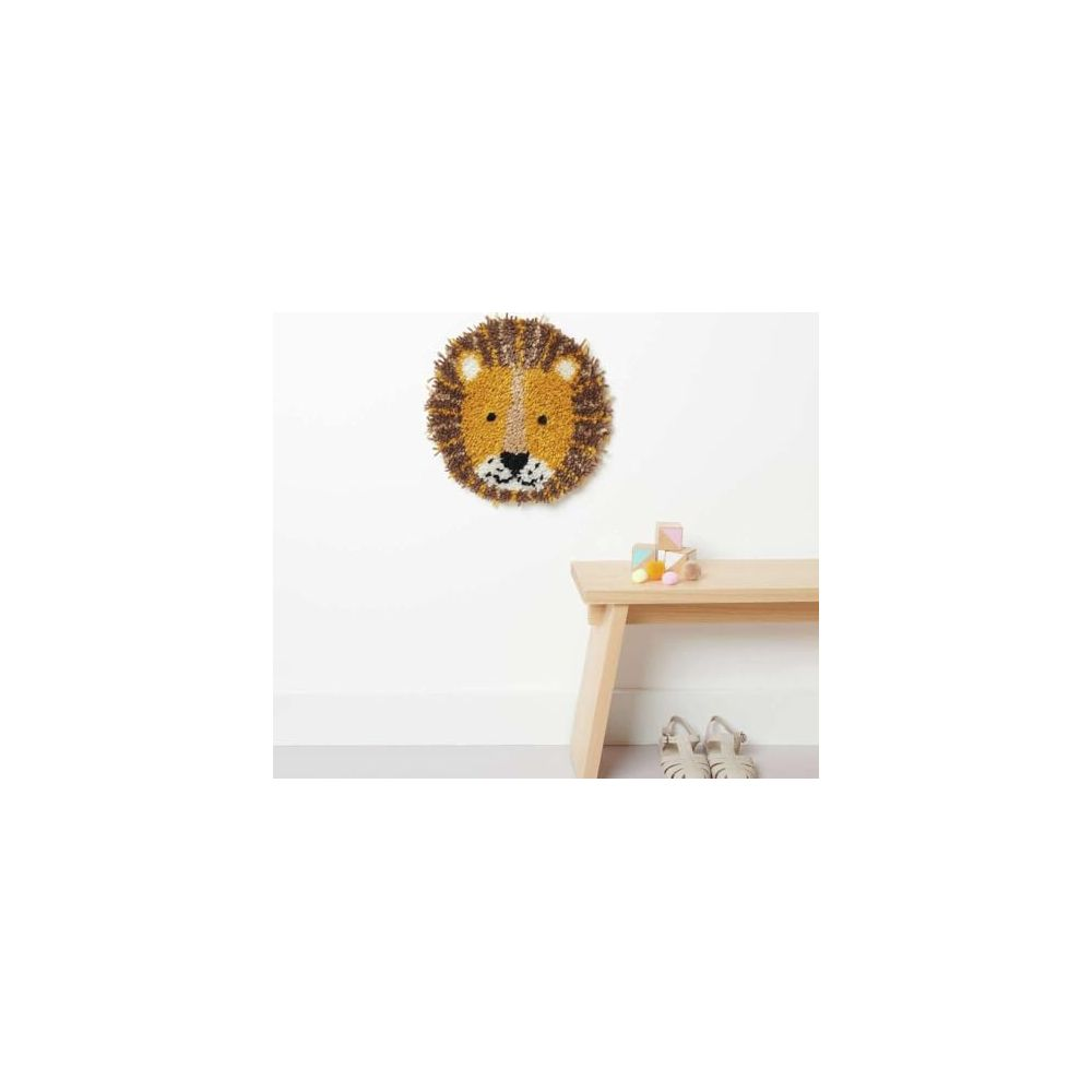 Ein flauschiger Löwen-Wandteppich hängt an einer weißen Wand über einer Holzbank mit Kinderschuhen und Bauklötzen.