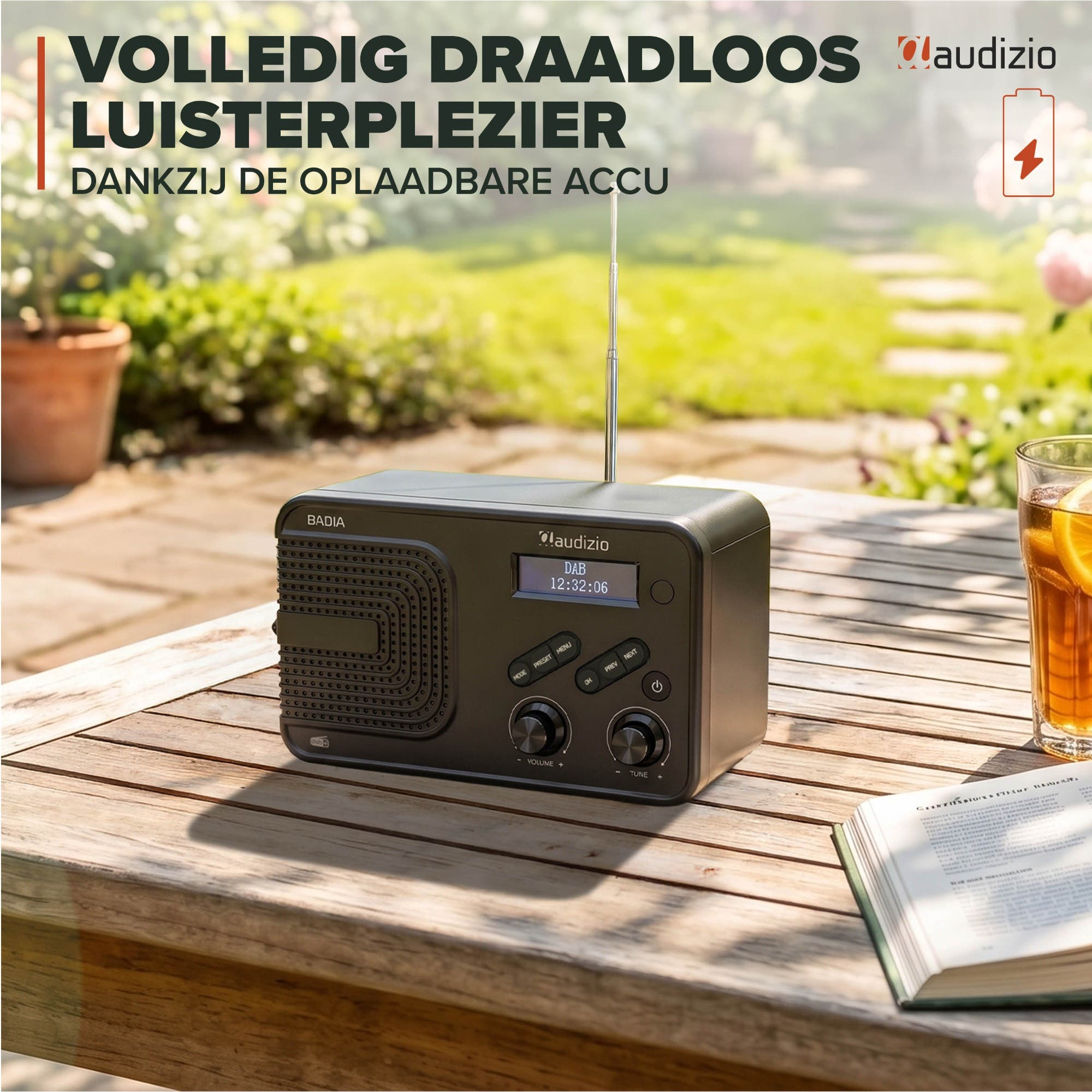 Una radio Audizio negra sobre una mesa de madera en el jardín, junto a un libro y un vaso de té helado.
