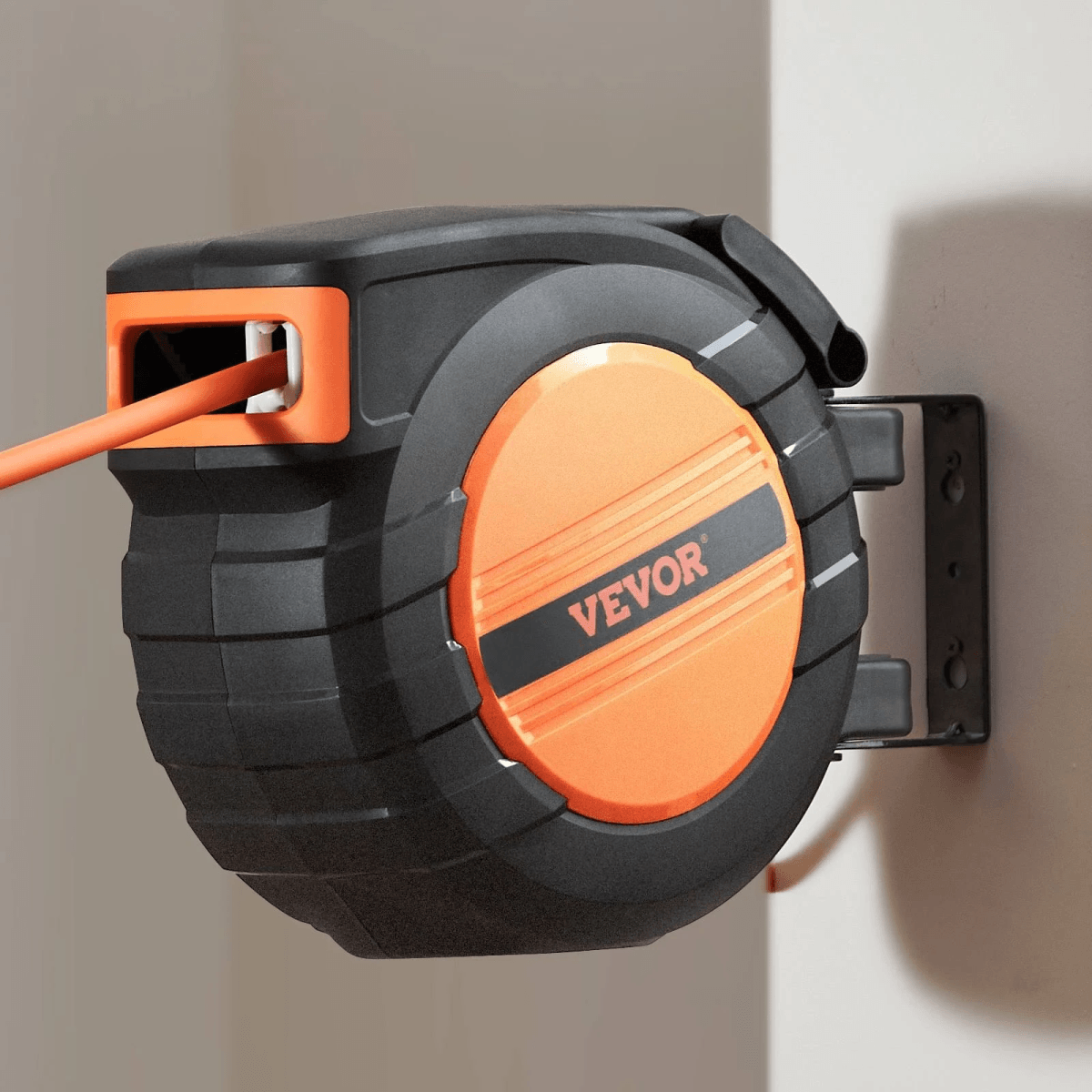 Un carrete de cable VEVOR negro y naranja montado en la pared con un cable naranja extendido.