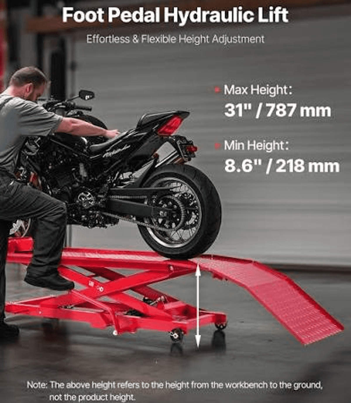 Un hombre empuja una motocicleta hacia una mesa elevadora hidráulica roja en un garaje.