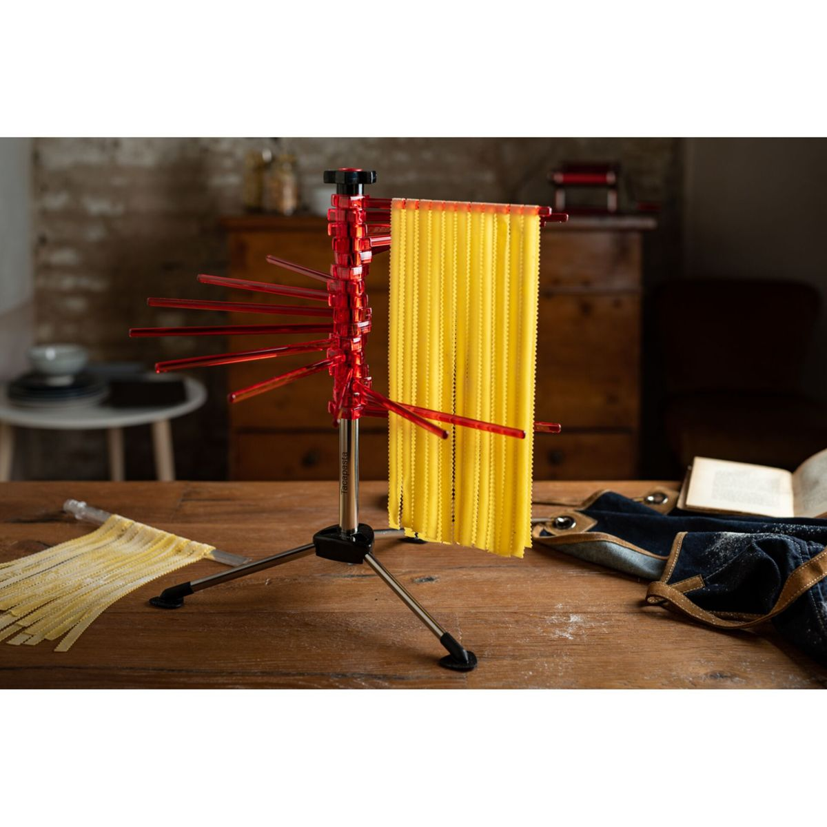 Uno stendi pasta rosso si trova su un tavolo di legno con pasta fresca.