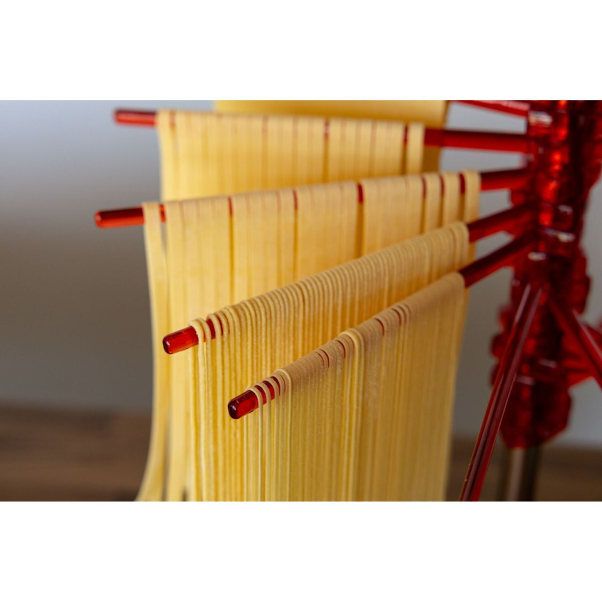 Pasta gialla fresca appesa ad asciugare su uno stendipasta rosso.