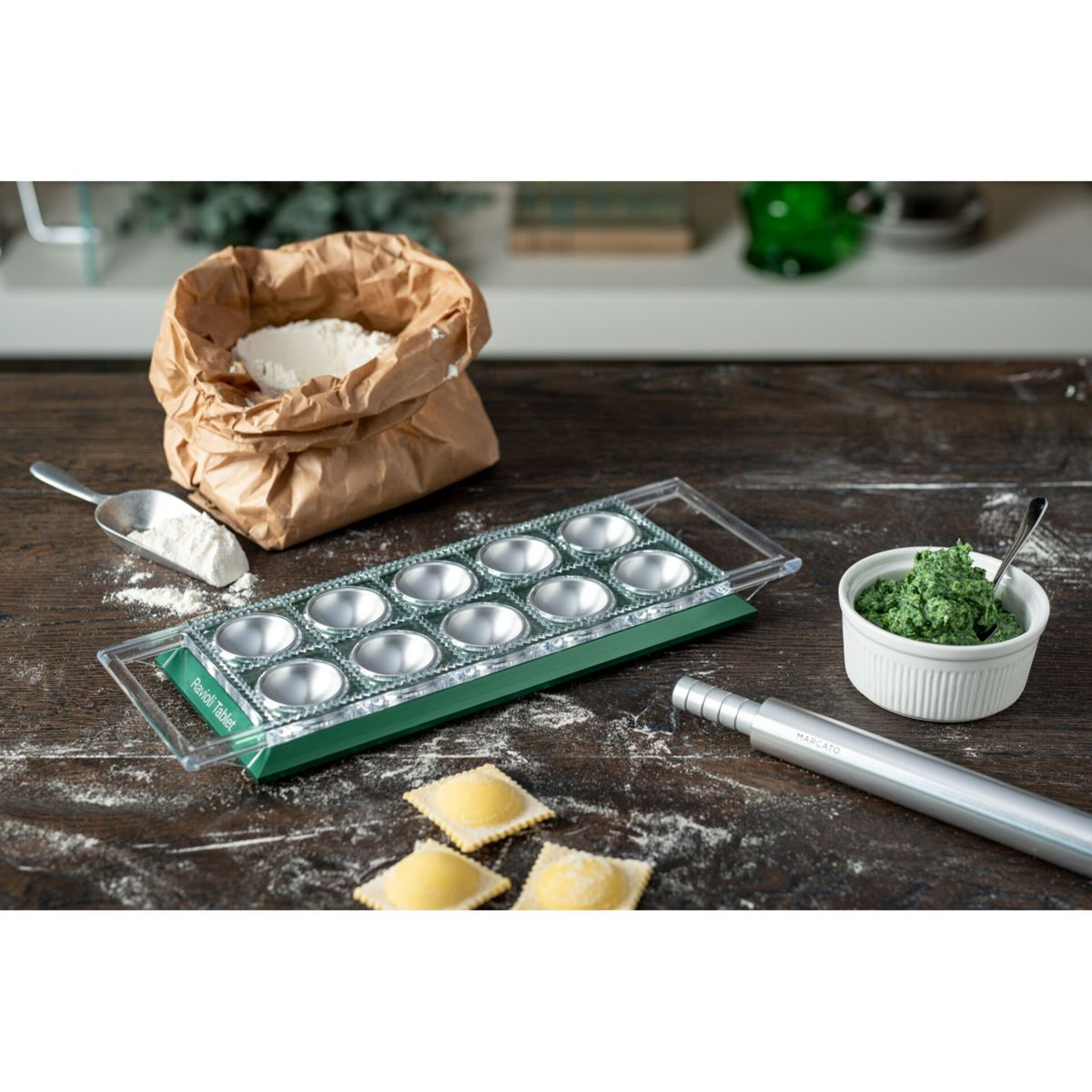 Ravioli-Tablett auf Holztisch mit Mehlbeutel, Teigfüllung, kleinem Nudelholz und zubereiteten Ravioli.