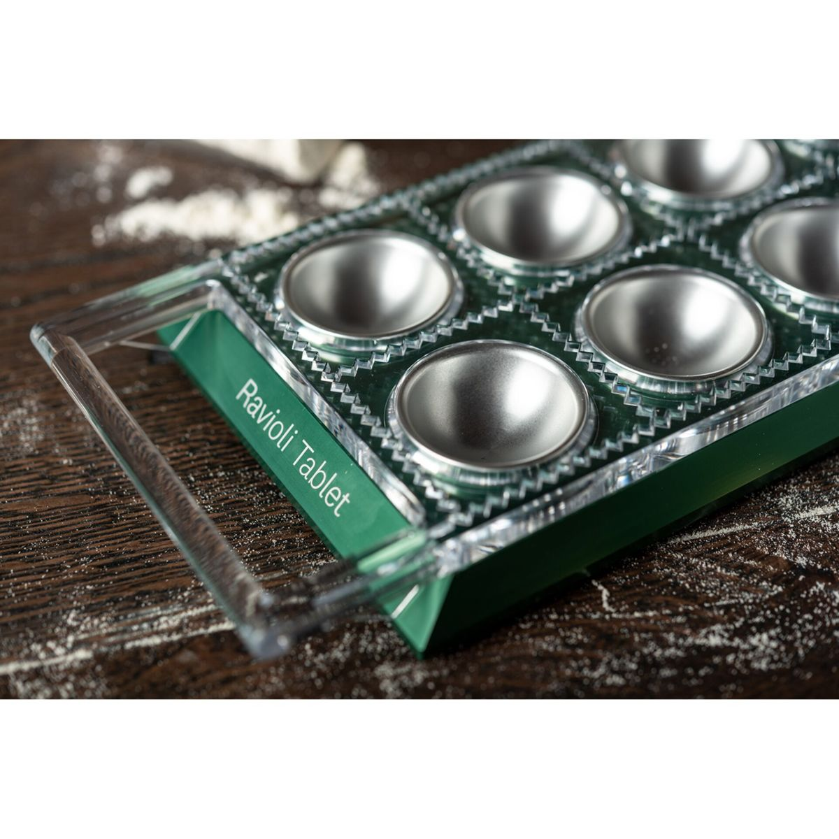 Eine grüne und klare Ravioli-Tablet-Form liegt auf einem dunklen Holztisch mit Mehl.