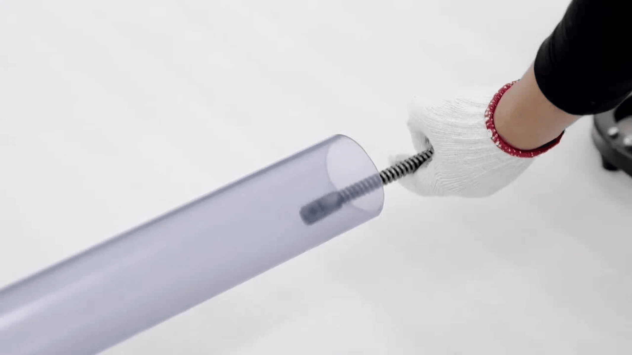 Una mano enguantada introduce un resorte largo y flexible en un tubo de plástico transparente.
