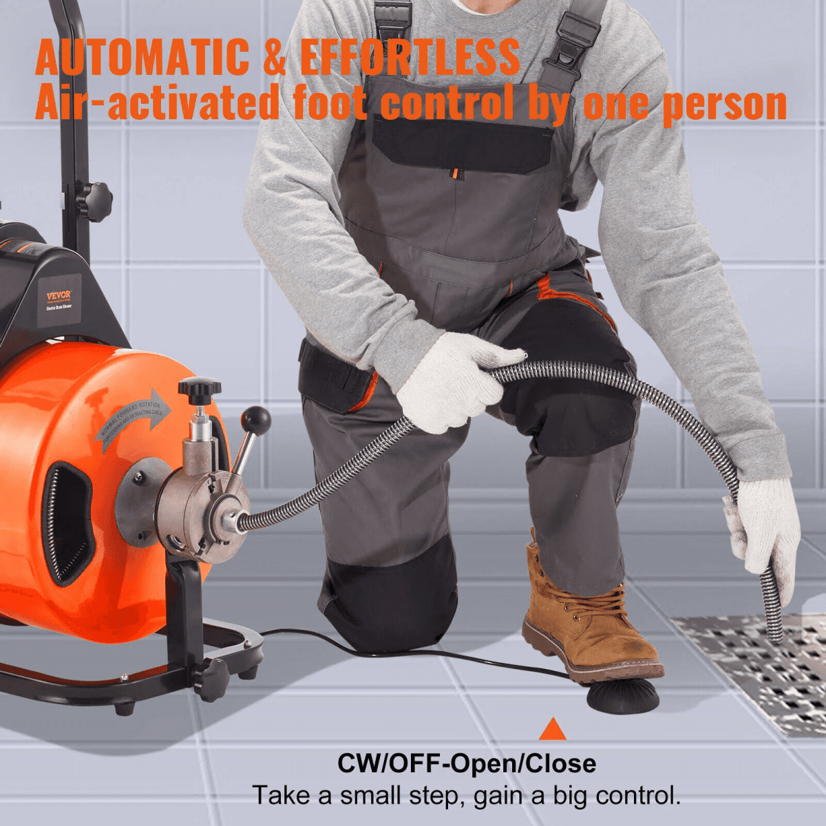 Un trabajador con mono gris usa un pedal para operar una máquina limpiatuberías eléctrica naranja.