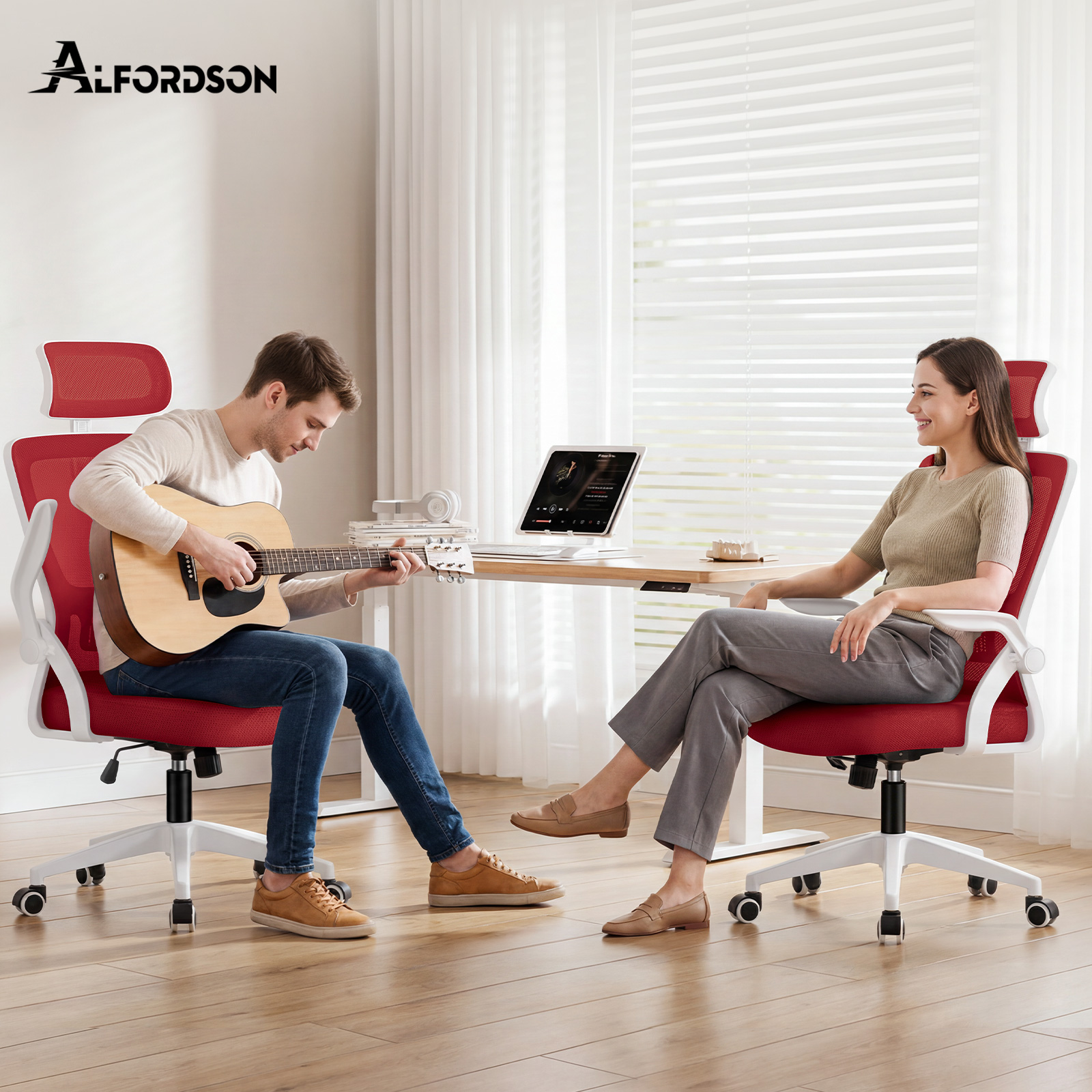 Ein Mann sitzt in einem roten Bürostuhl und spielt Gitarre, während eine Frau ihm in einem gleichen Stuhl gegenübersitzt.