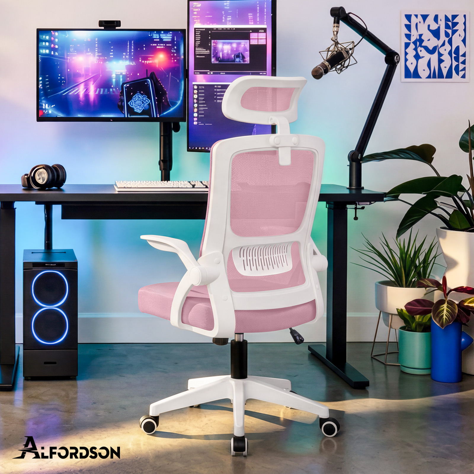 Ein rosa-weißer ergonomischer Gaming-Stuhl in einem hellen Raum mit zwei Monitoren, einem PC und Zimmerpflanzen.