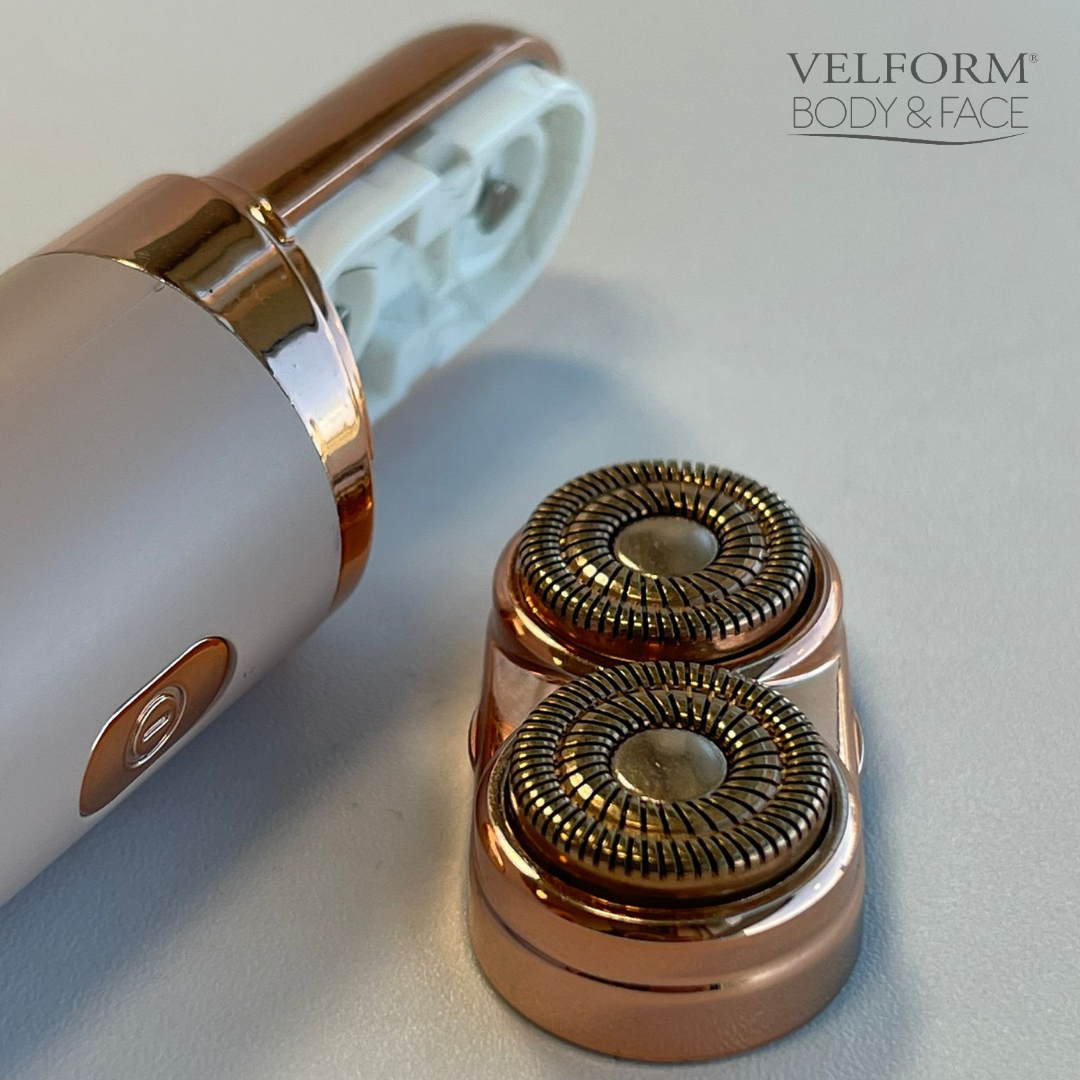 Rasoir Velform Body & Face or rose et blanc avec accessoire de lame double tête amovible sur surface claire.