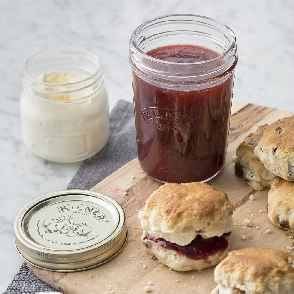 Scones mit Erdbeermarmelade und Clotted Cream in Gläsern auf einem Holzbrett.
