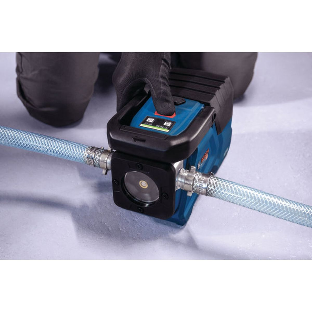 Eine glovierte Hand bedient eine blaue Bosch-Pumpe, die an transparente Schläuche angeschlossen ist.
