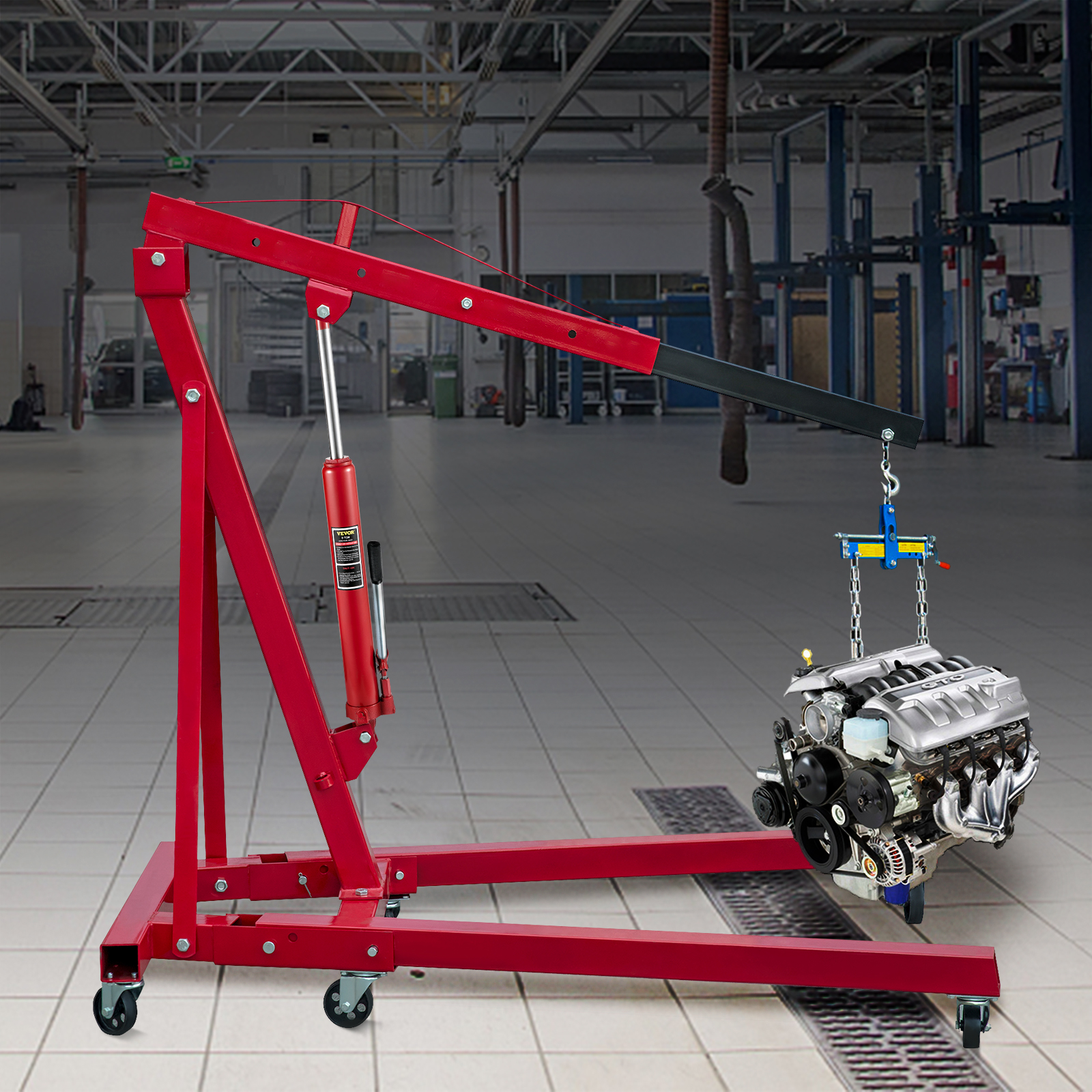 Una grúa roja para motores levanta el motor de un coche en un taller con suelo de baldosas.