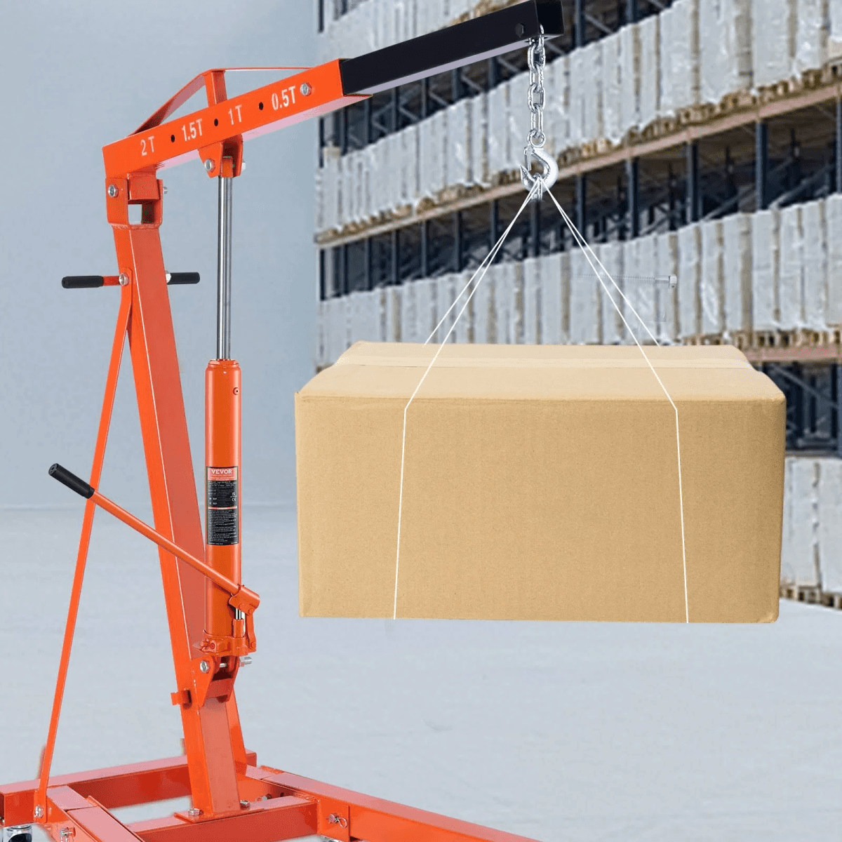 Una grúa hidráulica naranja levanta una caja grande de cartón en un almacén.