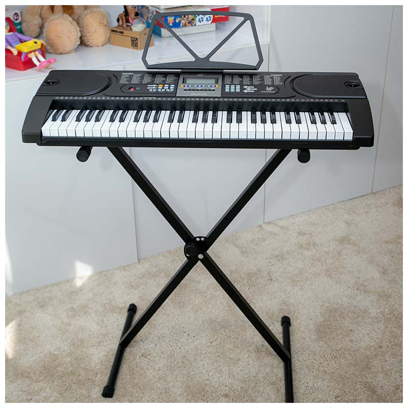 Ein schwarzes E-Keyboard auf einem X-Ständer vor einer weißen Wand mit Spielzeug im Hintergrund.