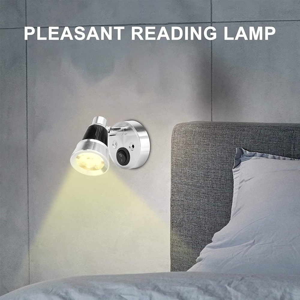 Eine silberne Wand-Leseleuchte ist an einer grauen Wand über einem Bett mit Kissen montiert und strahlt warmes Licht aus.