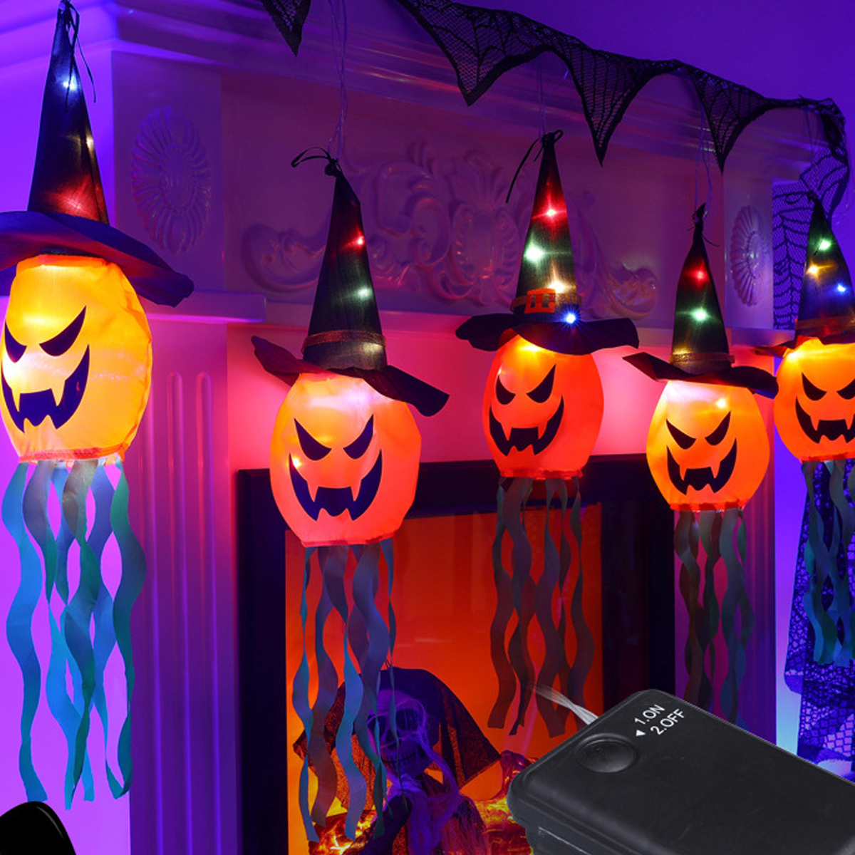 Leuchtende Halloween-Kürbislaternen mit Hexenhüten und grünen Bändern hängen an einem Kamin.