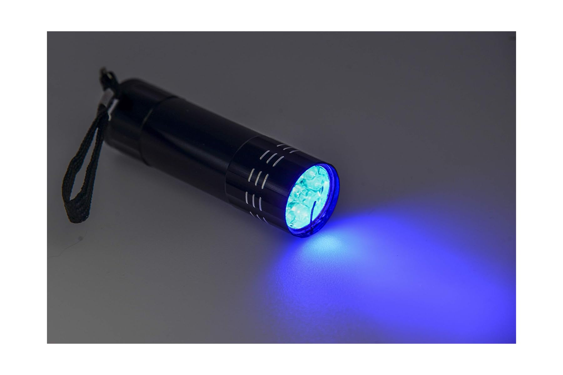 Eine kleine schwarze UV-Taschenlampe leuchtet auf einer grauen Oberfläche blau.