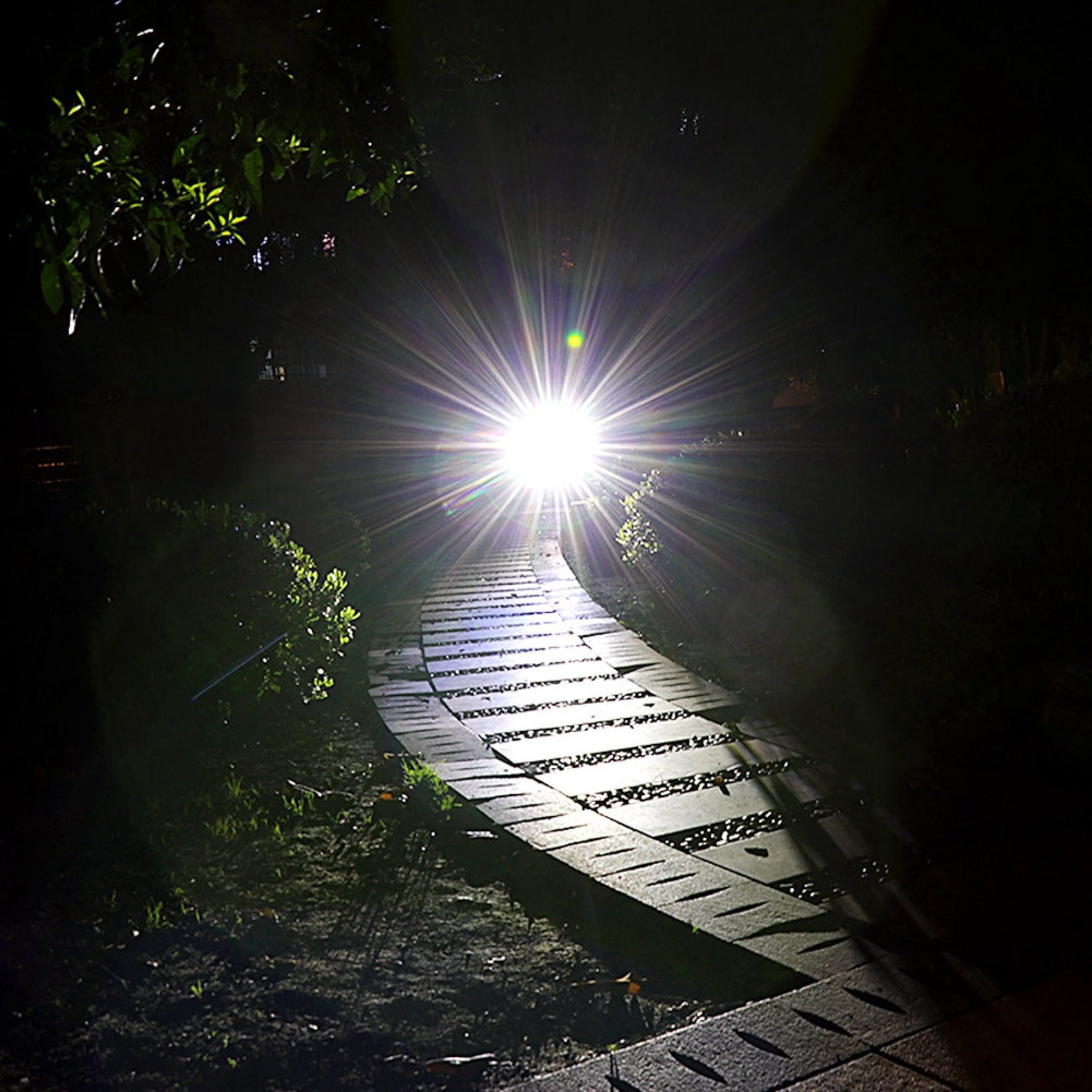 Ein hell erleuchteter, geschwungener Steinweg bei Nacht mit einer starken Lichtquelle am Ende.