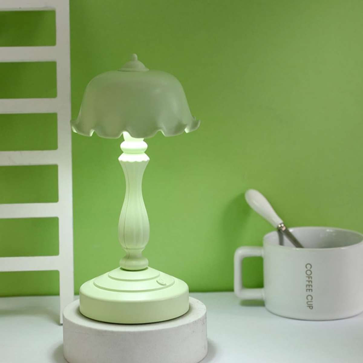 Eine grüne Tischlampe steht auf einer weißen Plattform neben einer weißen Tasse vor grünem Hintergrund.