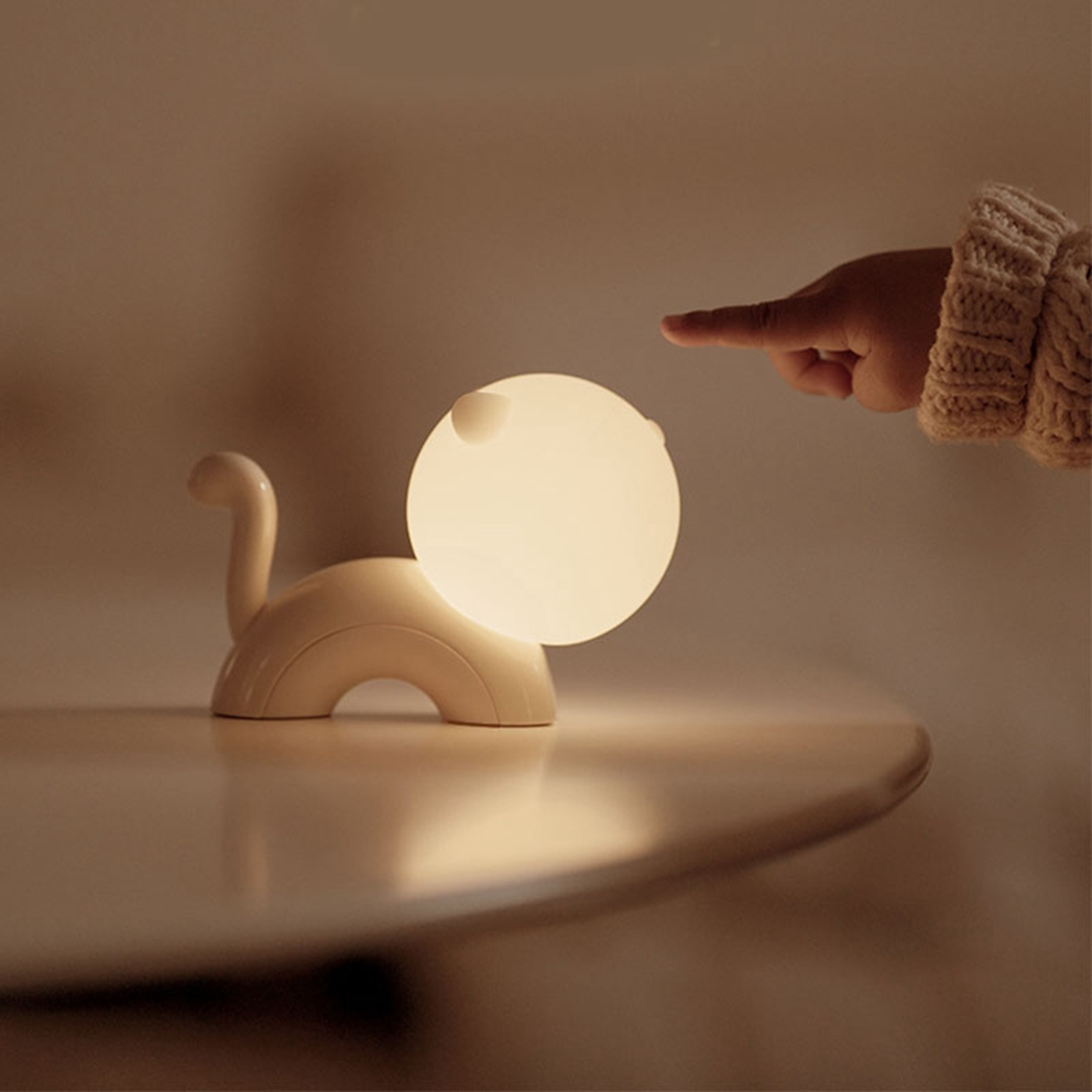 Eine kleine, helle Katzenlampe steht auf dem Tisch, während eine Hand danach greift.