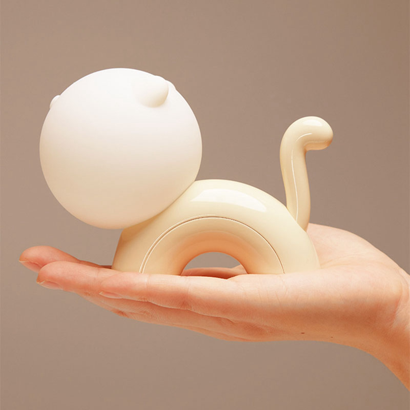 Eine Hand hält eine kleine, cremefarbene Katzenlampe mit rundem Kopf und aufrechtem Schwanz.