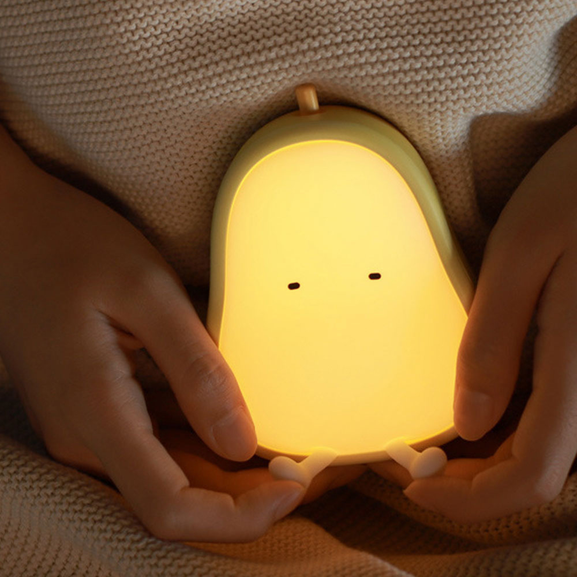 Person hält eine niedliche, gelbe Birnenlampe mit leuchtendem Licht.
