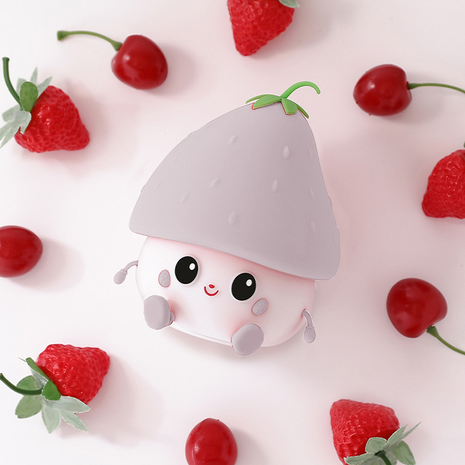 Ein süßer, puppenartiger Gegenstand mit Erdbeerhut und kawaii Gesicht, umgeben von echten Erdbeeren und Kirschen auf weißem Grund.
