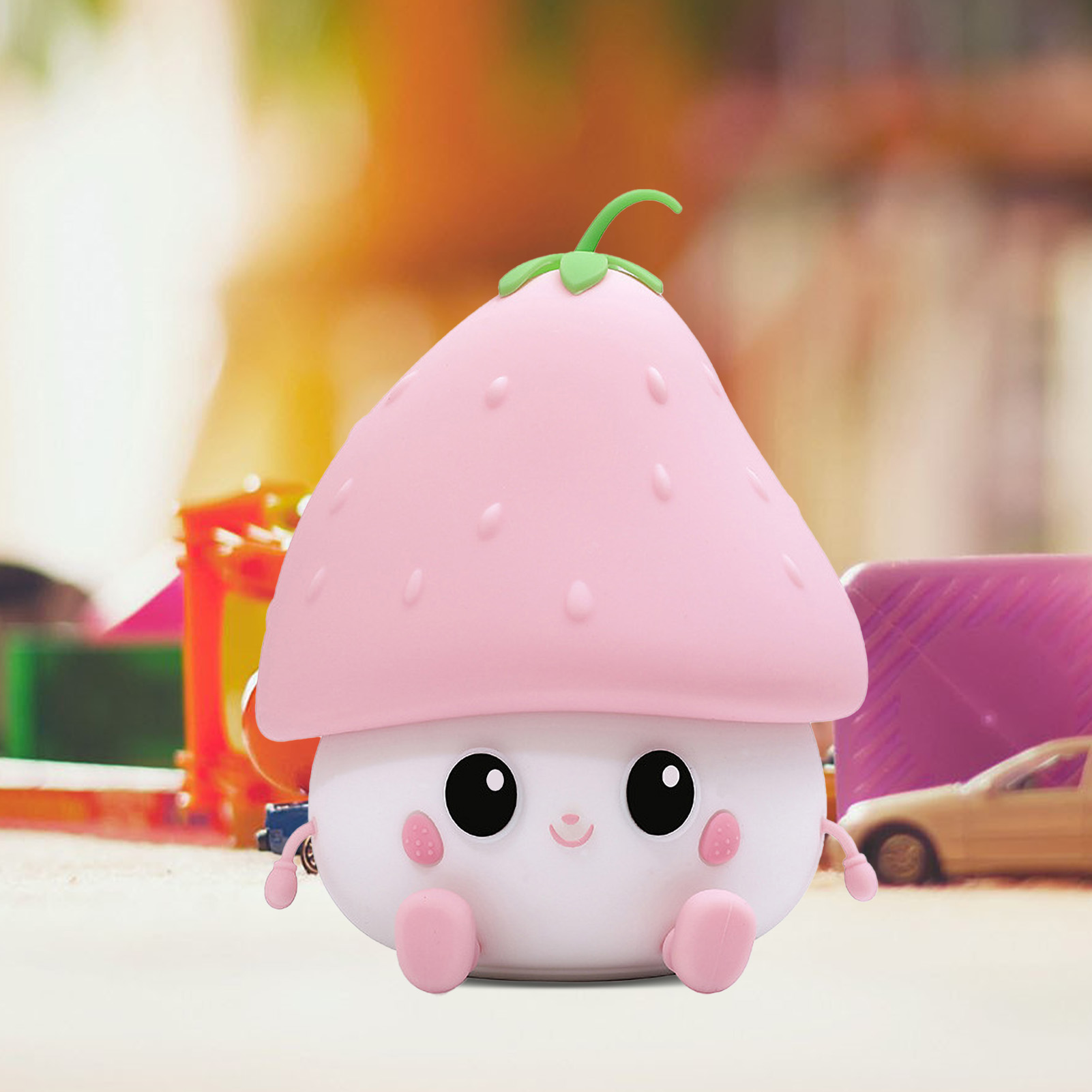 Eine rosafarbene erdbeerförmige Lampe mit süßem Gesicht und pinken Füßen sitzt vor verschwommenem Hintergrund.