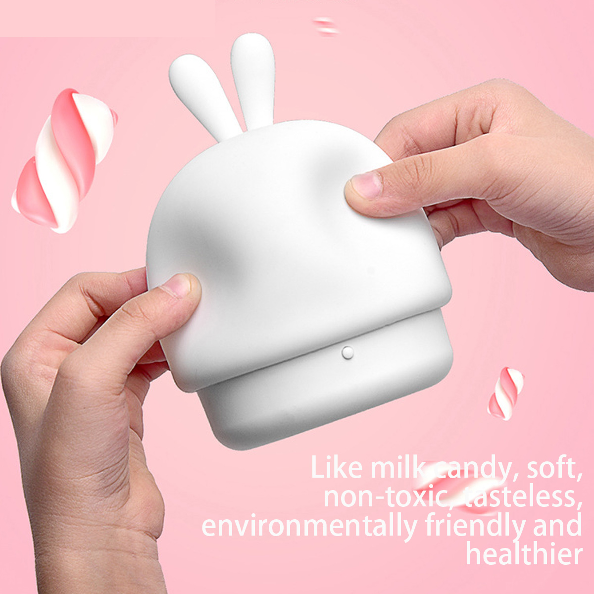 Hände drücken ein weißes, weiches, hasenförmiges Silikonobjekt vor rosa Hintergrund mit schwebenden Marshmallows.