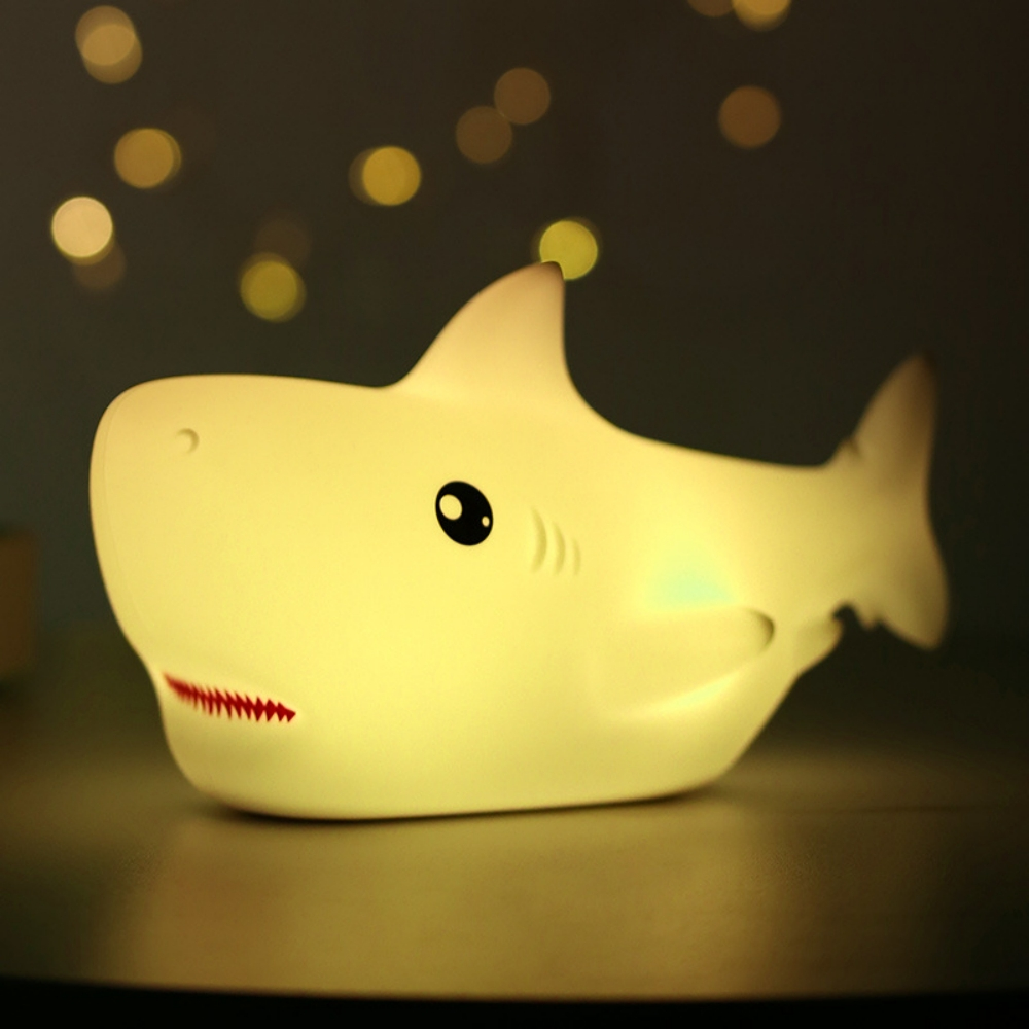 Eine weiße, leuchtende Haischlampe steht auf einer Oberfläche vor einem dunklen Hintergrund mit warmen Bokeh-Lichtern.