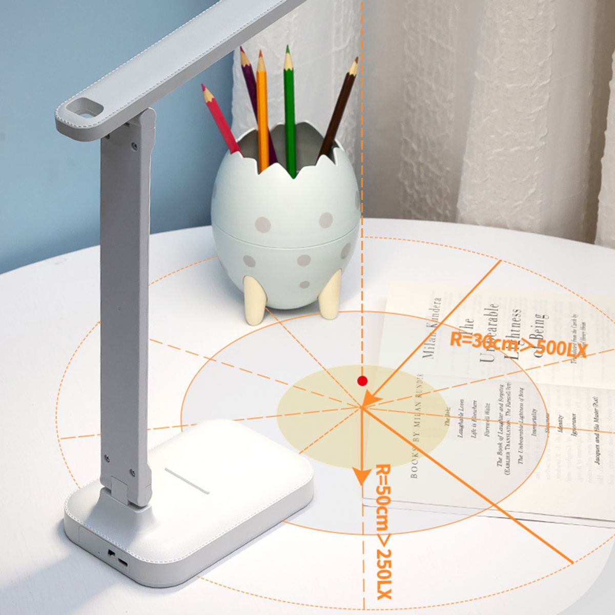 Eine weiße Schreibtischlampe, ein Eierbecher mit Buntstiften und ein Buch mit orangen Reichweitendiagrammen auf dem Tisch.
