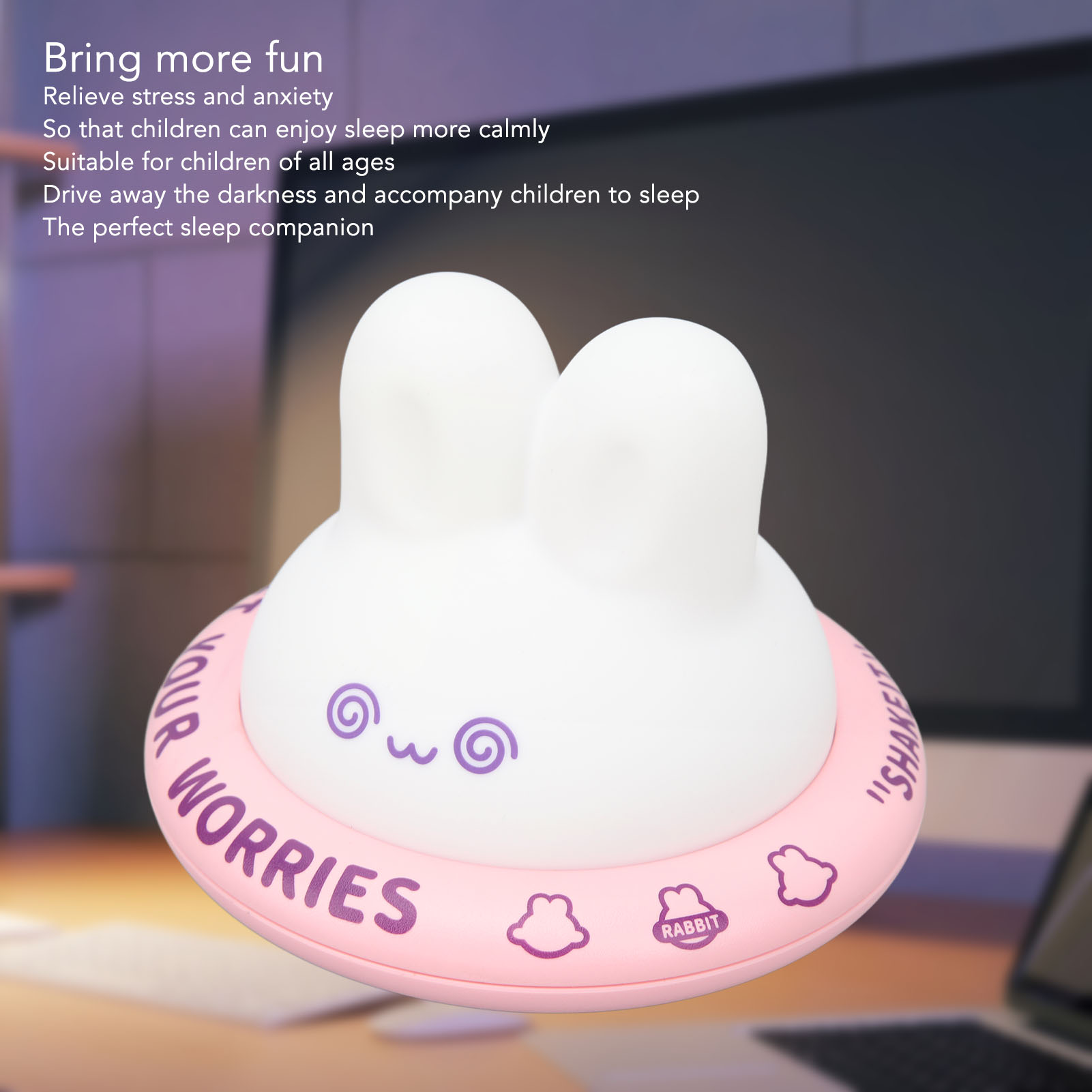 Eine weiße, hasenförmige Nachtlampe mit rosa Ring, auf dem "WORRIES" und Hasen-Symbole stehen, vor einem Schreibtisch.