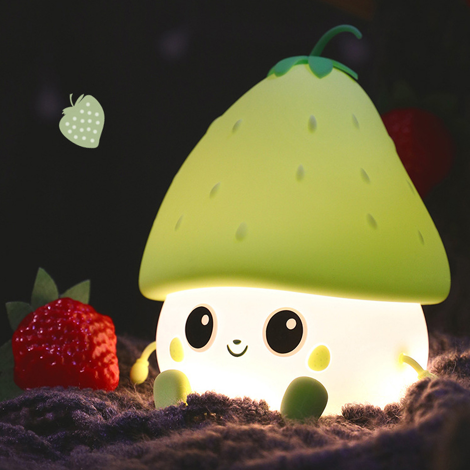 Ein süßes, leuchtendes erdbeerförmiges Nachtlicht auf einer Decke, flankiert von echten Erdbeeren.